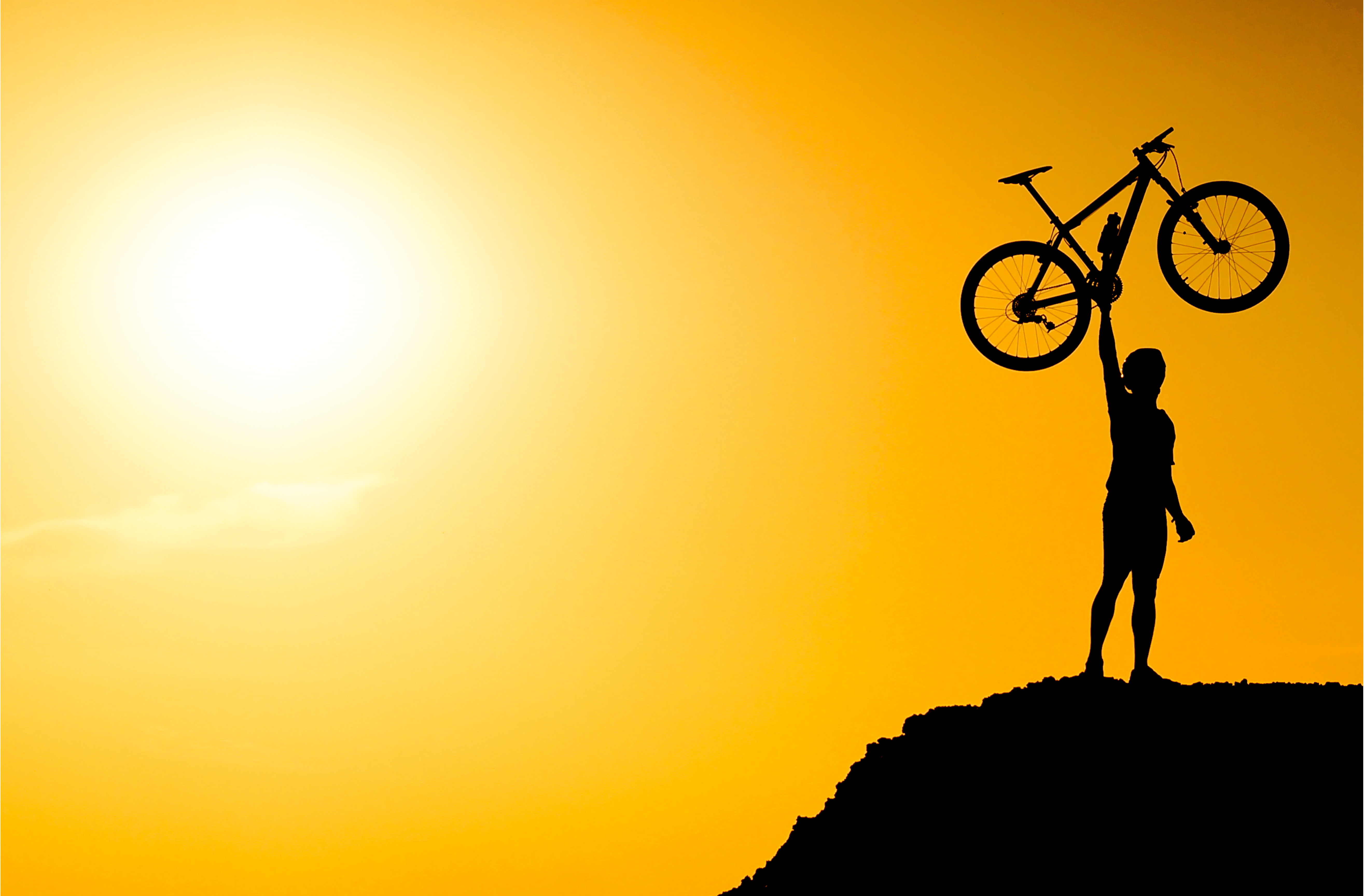 a man lifting a bicycle in the air with one hand on the edge of a mountain with the sun behind him