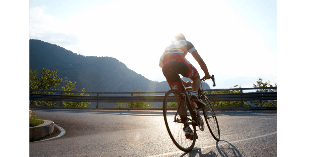 a man cycling a road bike around a bend with mountains in the distance