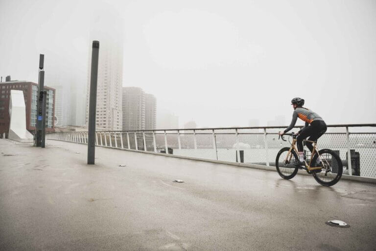 a woman cycling over a wet bridge in a city in the background