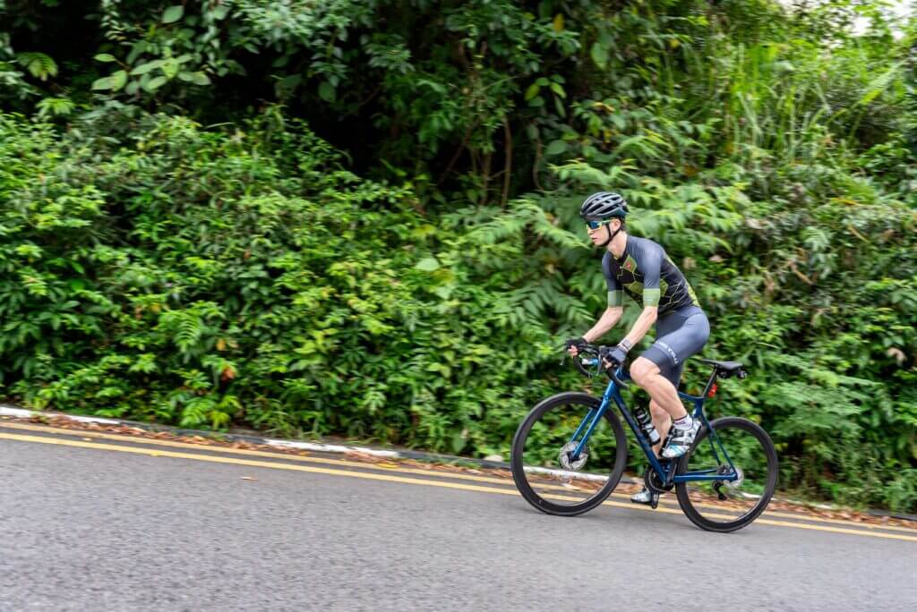a male cyclist cycling up a hill on a road bike, with trees behind him