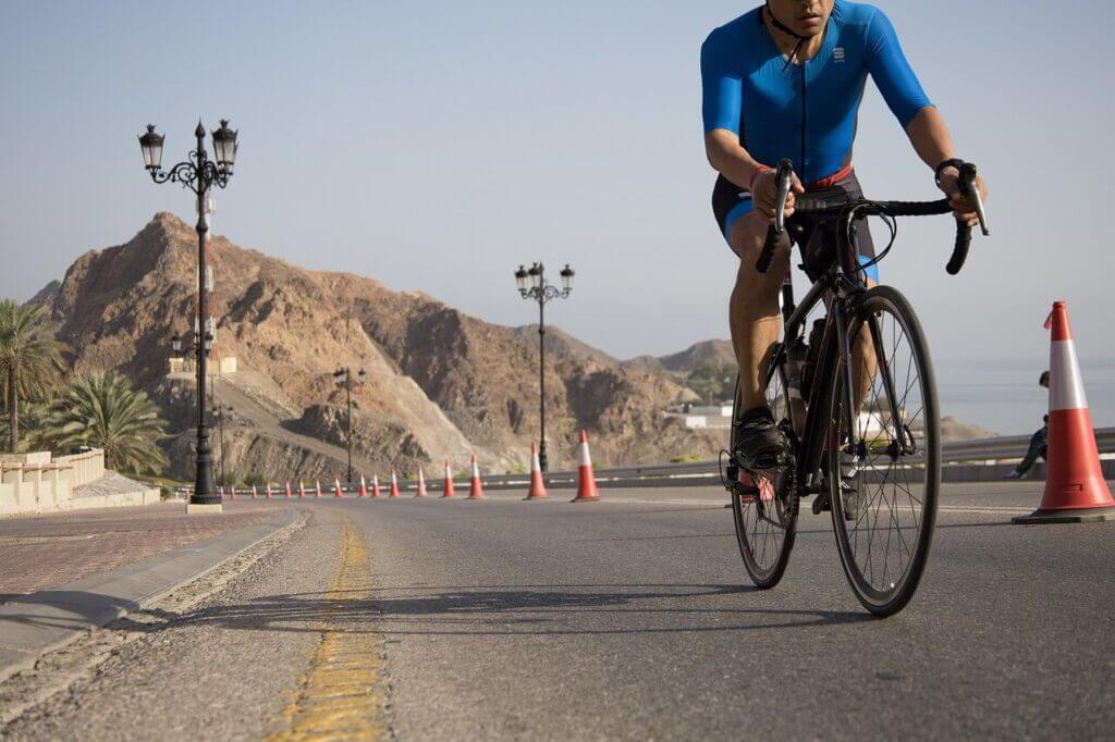 a competitive male cyclist cycling on a road with mountains and a clear sunny sky in the background.