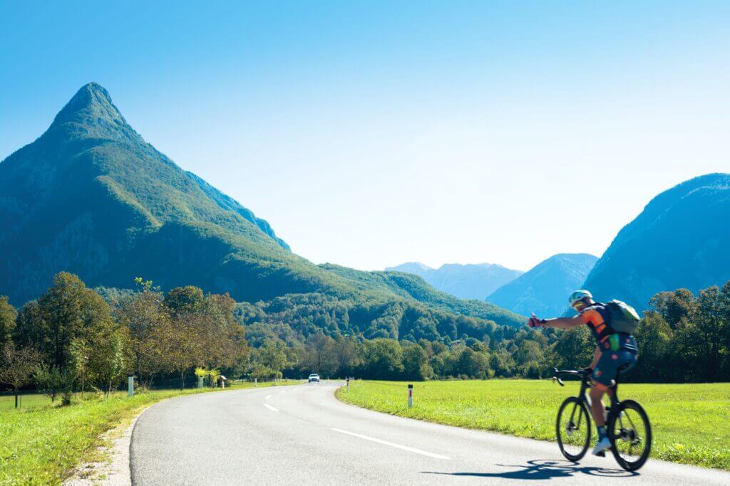 a man cycling on a road with mountains in the distance