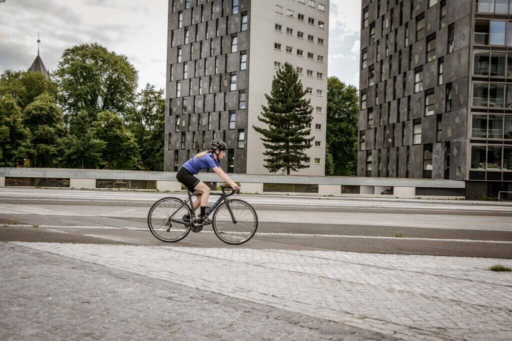 a female cyclist cycling on a road with tall buildings behind