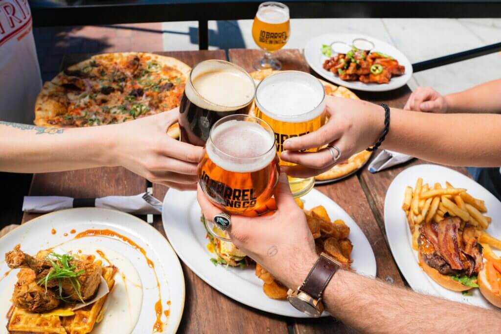 a group of people sitting down for dinner, make a toast with glasses of beer