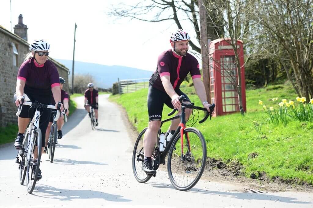 Group of cyclists riding through a country village smiling having fun in matching maroon jerseys