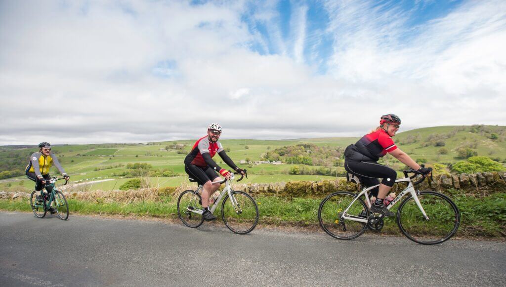 Three cyclists going up a hill in the Yorkshire countryside smiling