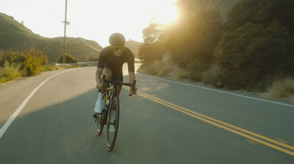 a cyclist goes around a bend in the road, with the sun shining behind him