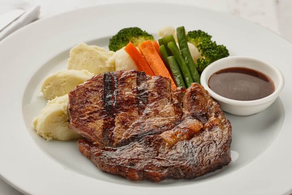 steak on a plate with mashed potatoes, vegetables and a sauce