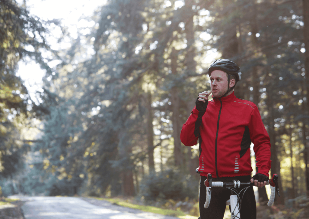 a male cyclist stopped eating some food, with trees behind him