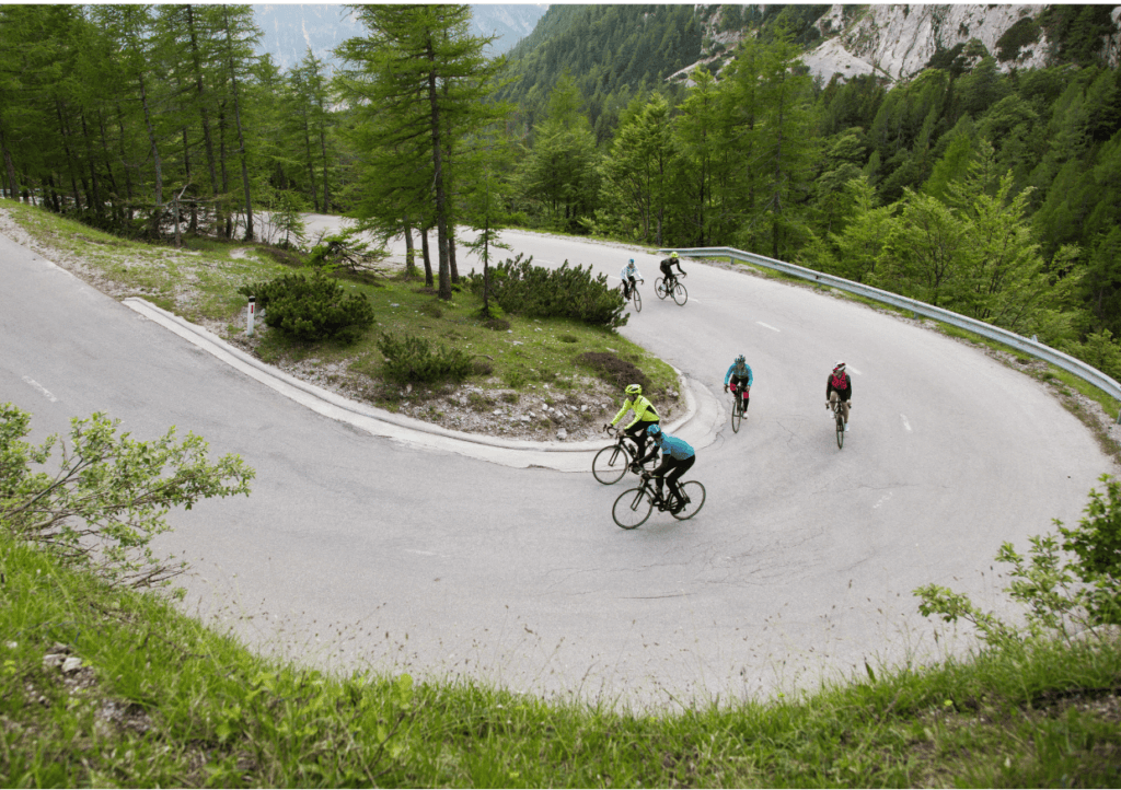 a group of cyclists going uphill around a bend, with mountains and trees in the background