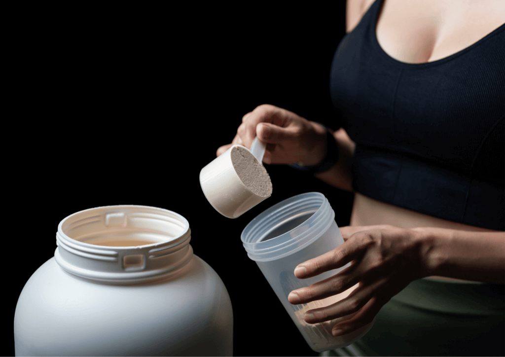 a woman scooping whey protein powder from a tub to make a protein drink