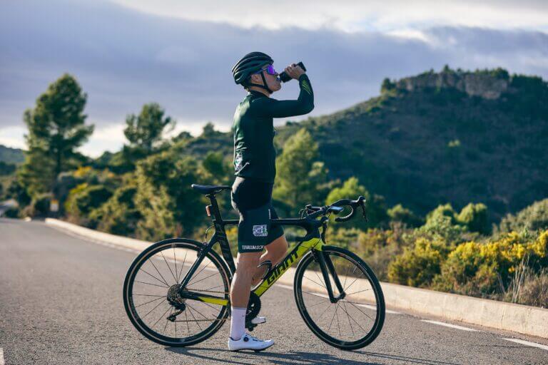 a cyclist stopped on the middle of the road drinking from a bottle