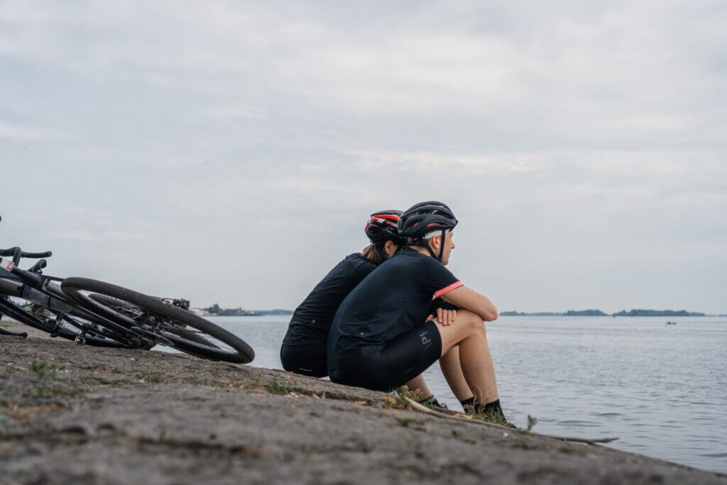 a man and women road cyclists sitting beside water looking out