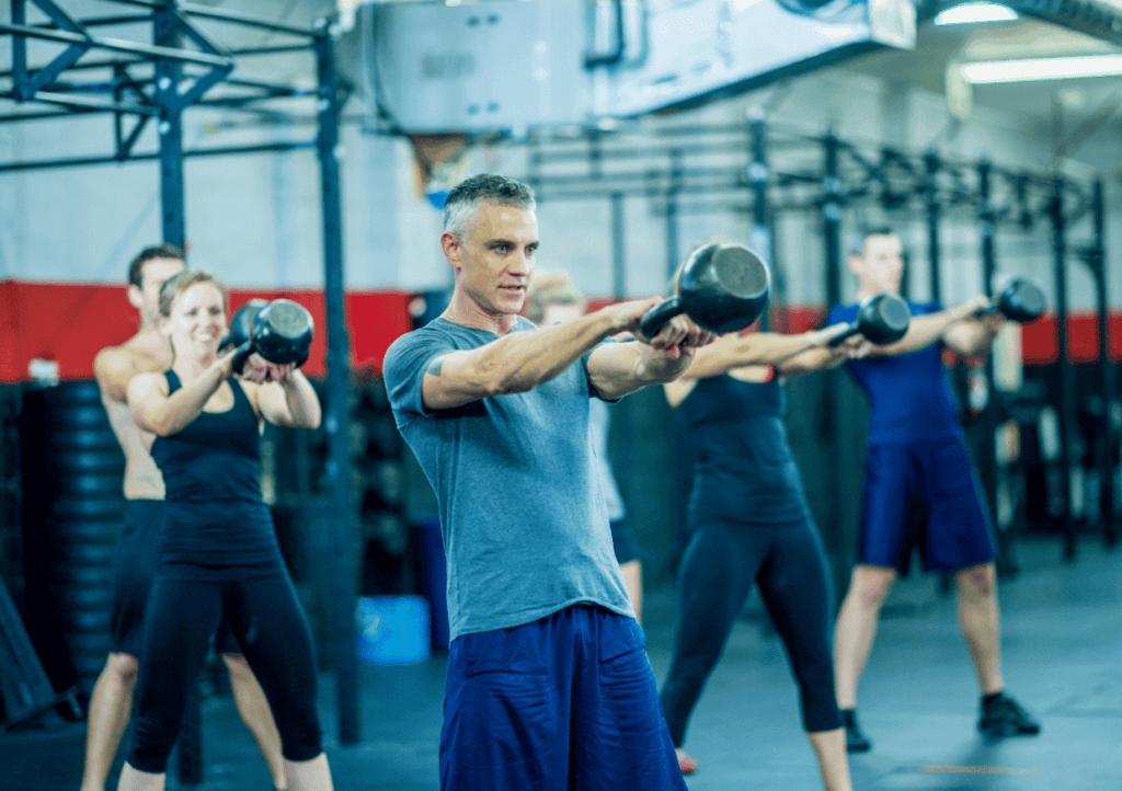 A group of men and woman in a fitness class, lifting kettlebells for strength training