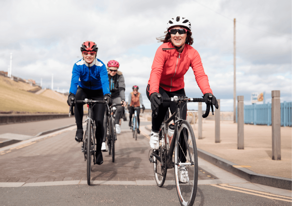 a group of female cyclists smiling as they ride their bikes on the road