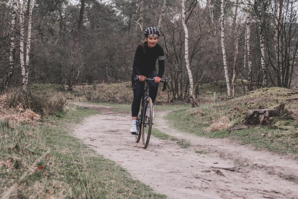 a female cyclist riding a gravel bike on a dirt road throw a forest