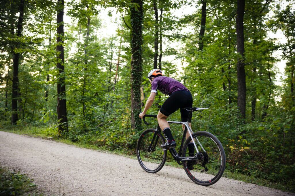 a male cyclist riding a gravel bike up a gravel road