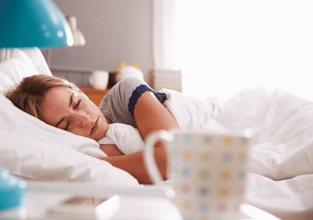 a woman in bed asleep, with a mug beside the bed