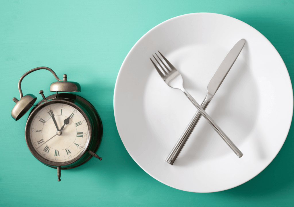 an empty plate with an alarm clock signifying the concept of fasting