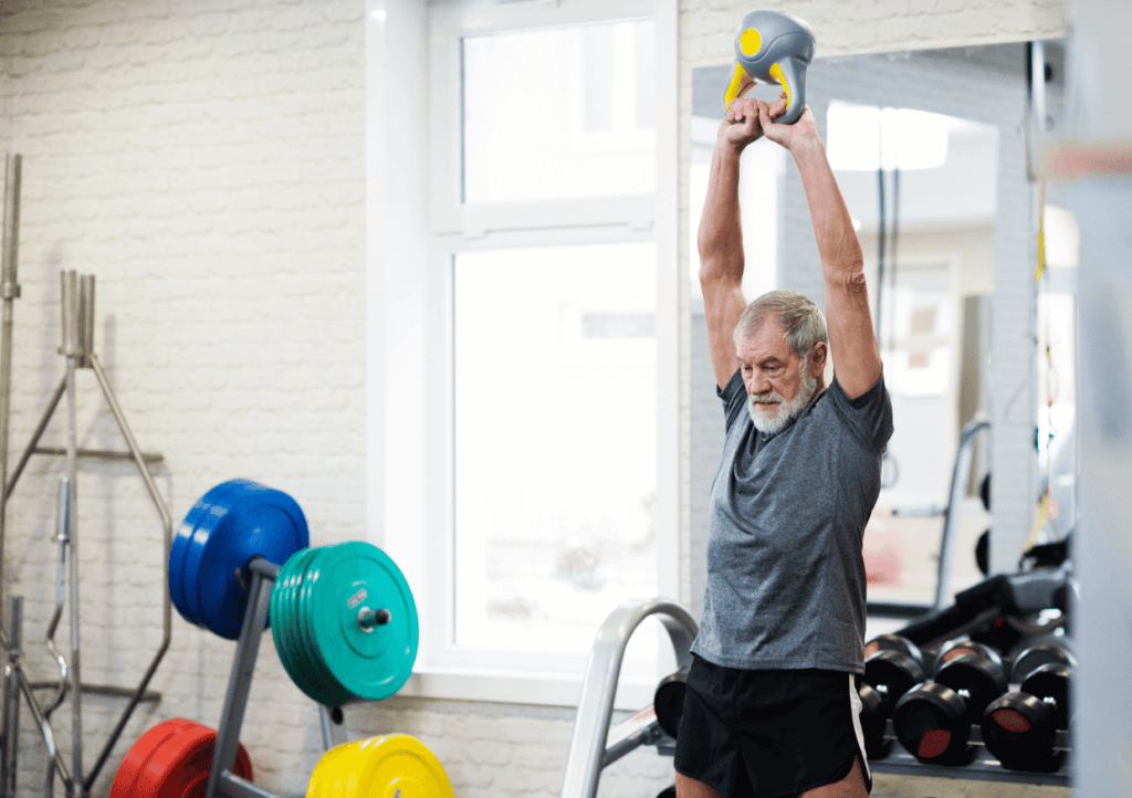 an older man lifting a kettlebell above his head in a gym