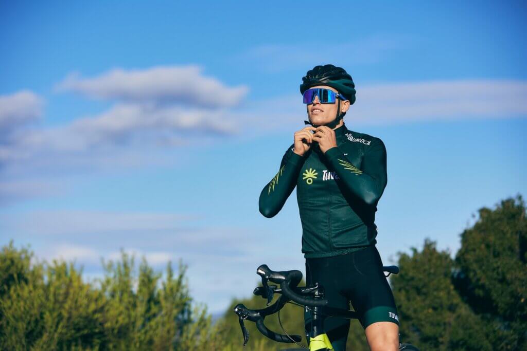 a man standing next to a bike in a field, putting on a helmet