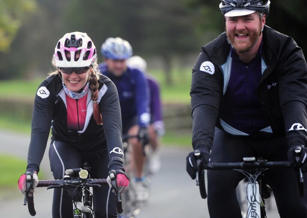 A male and female cyclist smiling and chatting riding along a country lane
