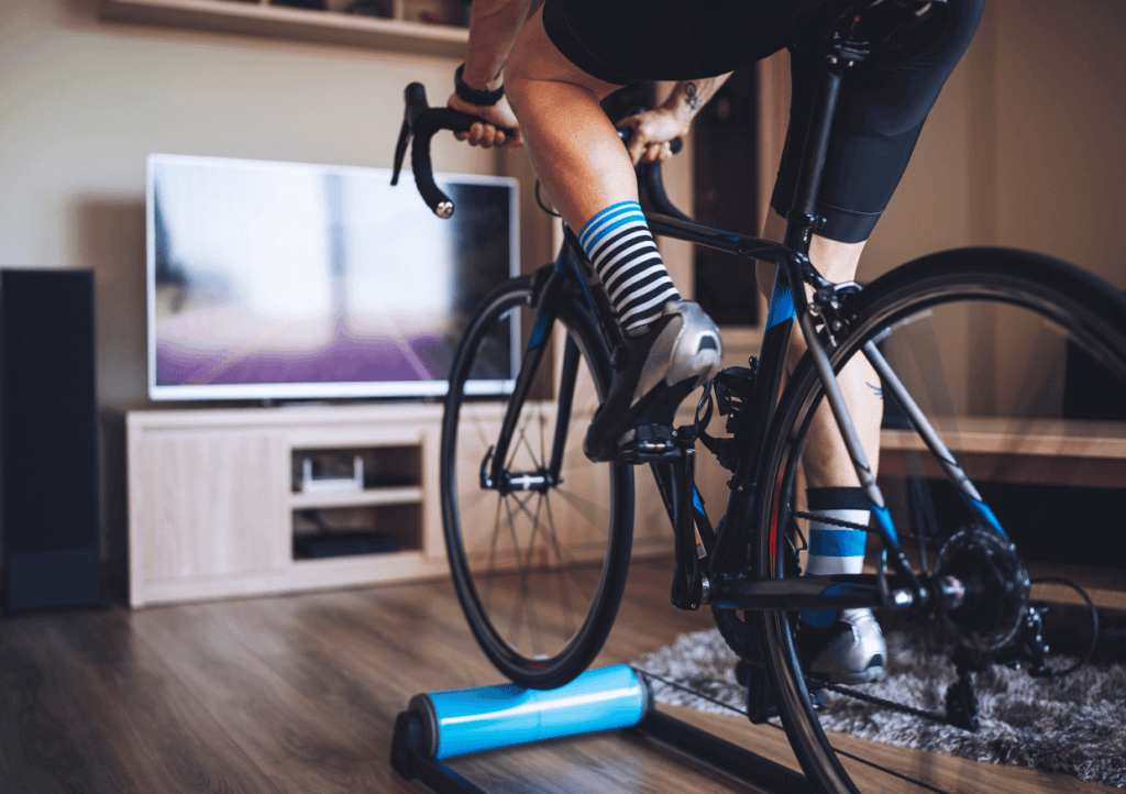 a man cycling indoors on  a bike rollers, in front of the tv