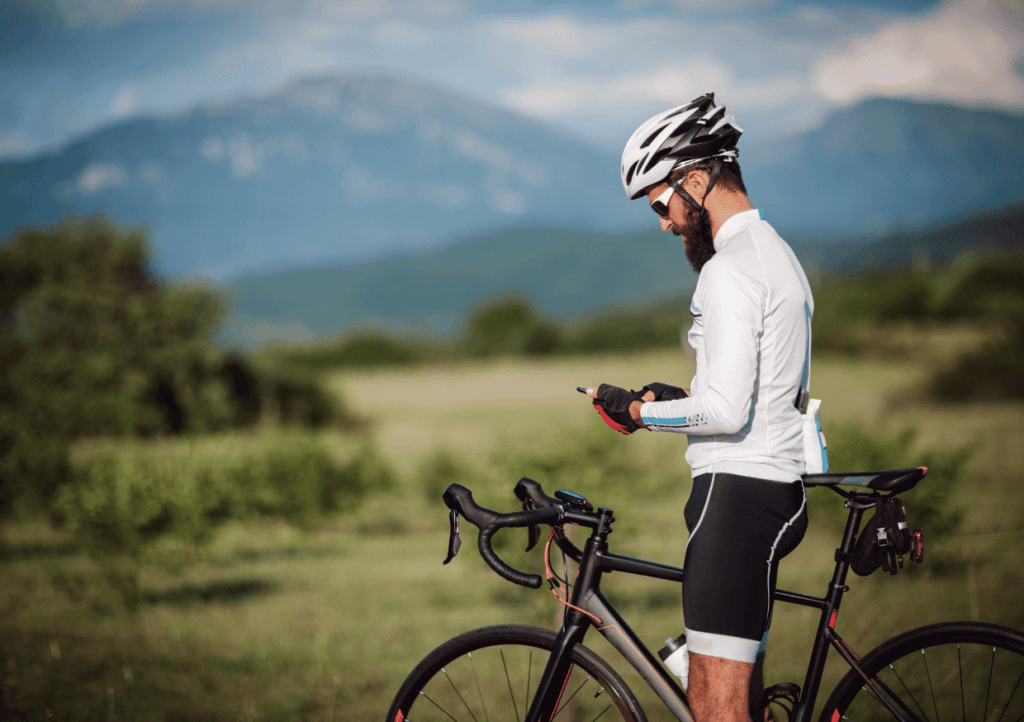 a stopped cyclist looking at his phone, with fields and mountains in the background.