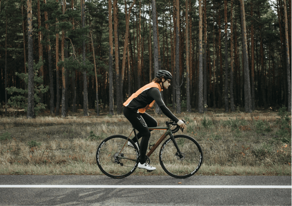 a man cycling a road bike along a road, with a forest of trees behind him