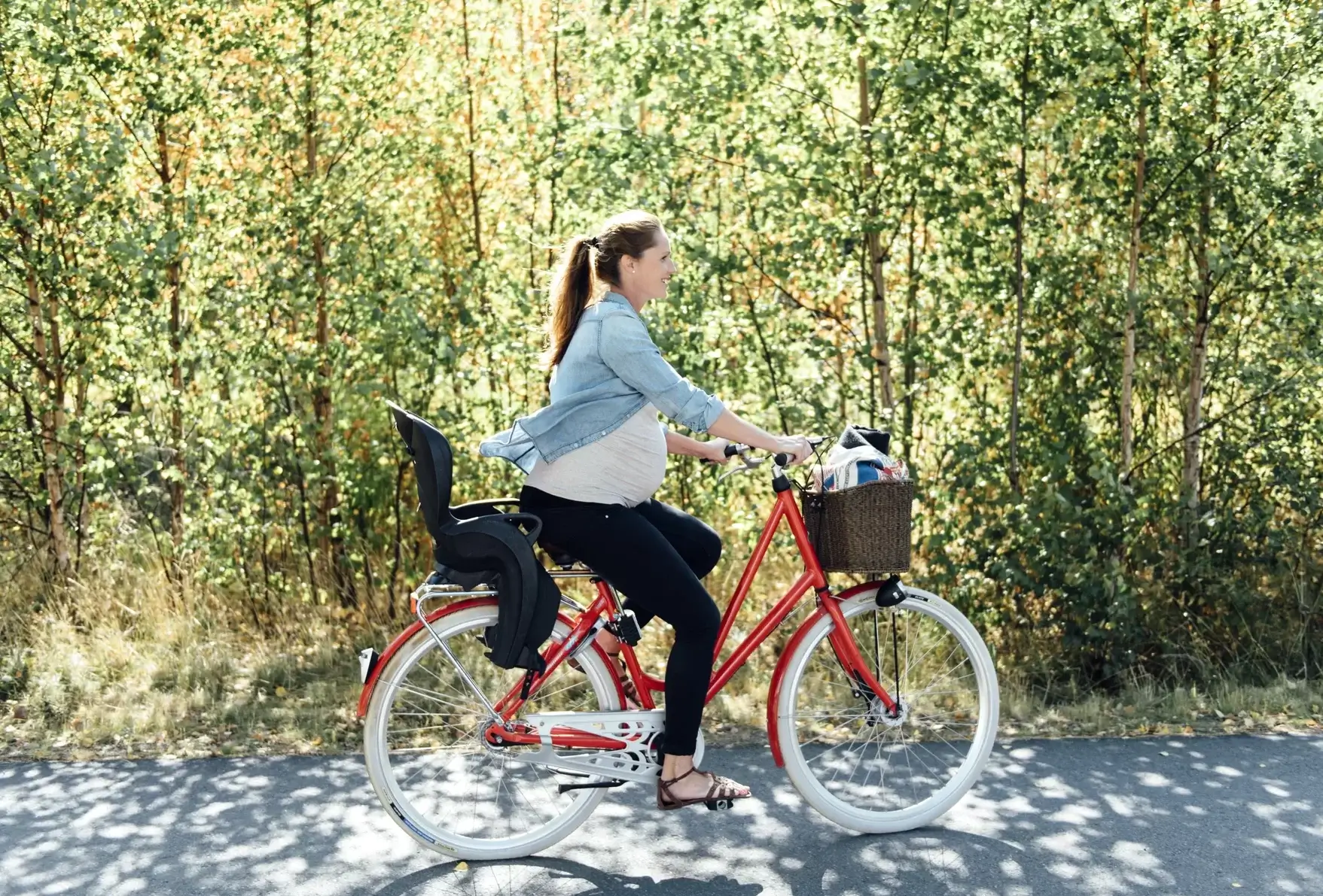 a pregnant woman cycling a bike along a tree lined road